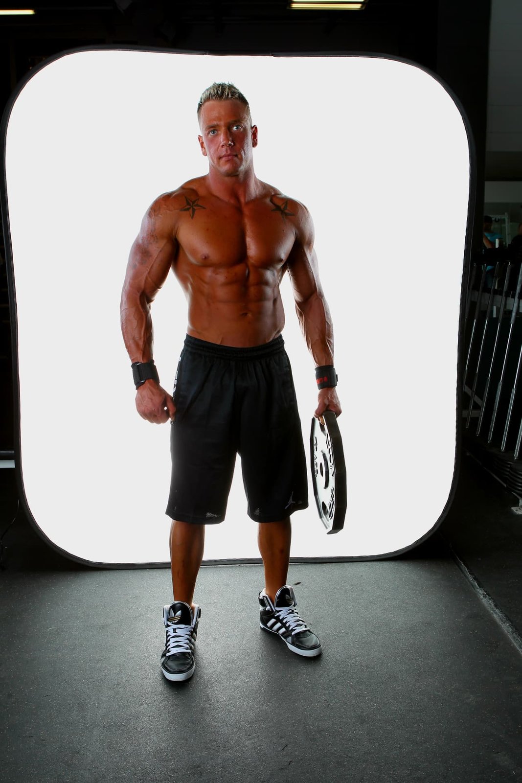 Online fitness coach Robert Agarand standing full-length in a gym studio holding a weight plate