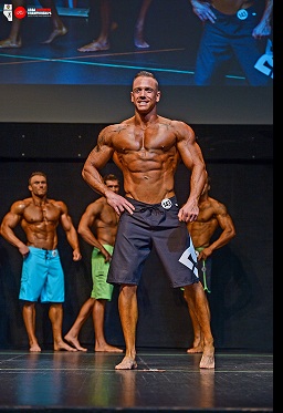 Coach Robert Agarand competing on stage in a Men's Physique bodybuilding competition